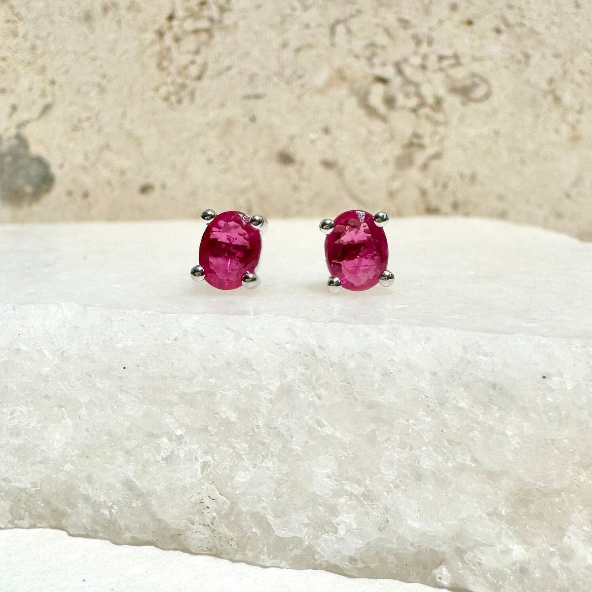 May include: A pair of oval-shaped ruby earrings with silver settings. The earrings are set against a white background.