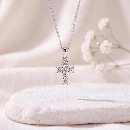 May include: A silver-toned necklace featuring a cross-shaped pendant. The cross is adorned with multiple small, clear, round-cut stones set in a prong setting. The pendant hangs from a delicate, thin silver-toned chain with a simple link design.