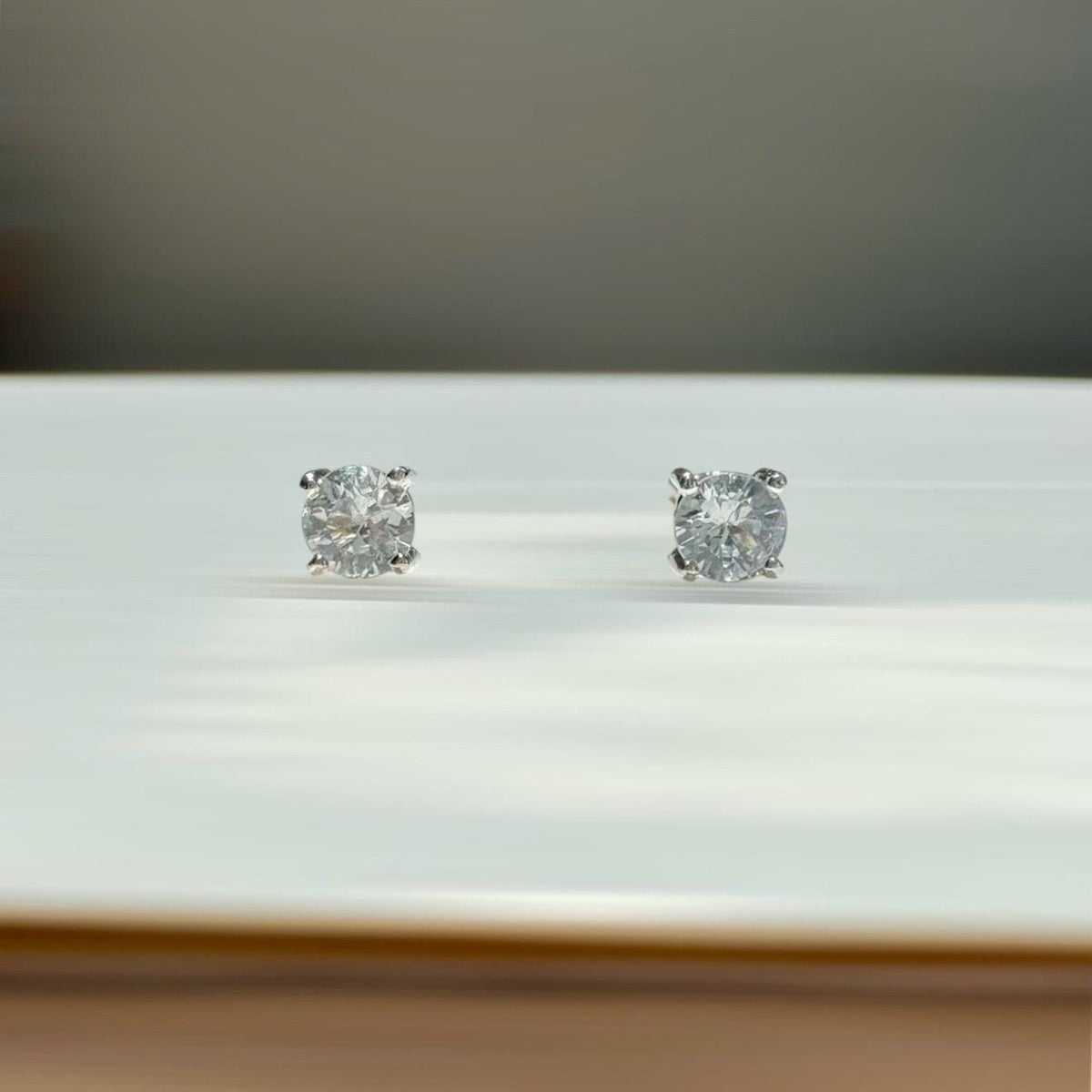 May include: A pair of diamond stud earrings. Each earring features a round, brilliant-cut diamond set in a silver-colored metal. The diamonds sparkle against a white background.