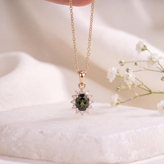 May include: A gold-toned necklace featuring a central oval-shaped dark green gemstone surrounded by a halo of small, clear, sparkling stones. The pendant is suspended from a delicate gold-toned chain, creating a refined and classic jewelry piece.