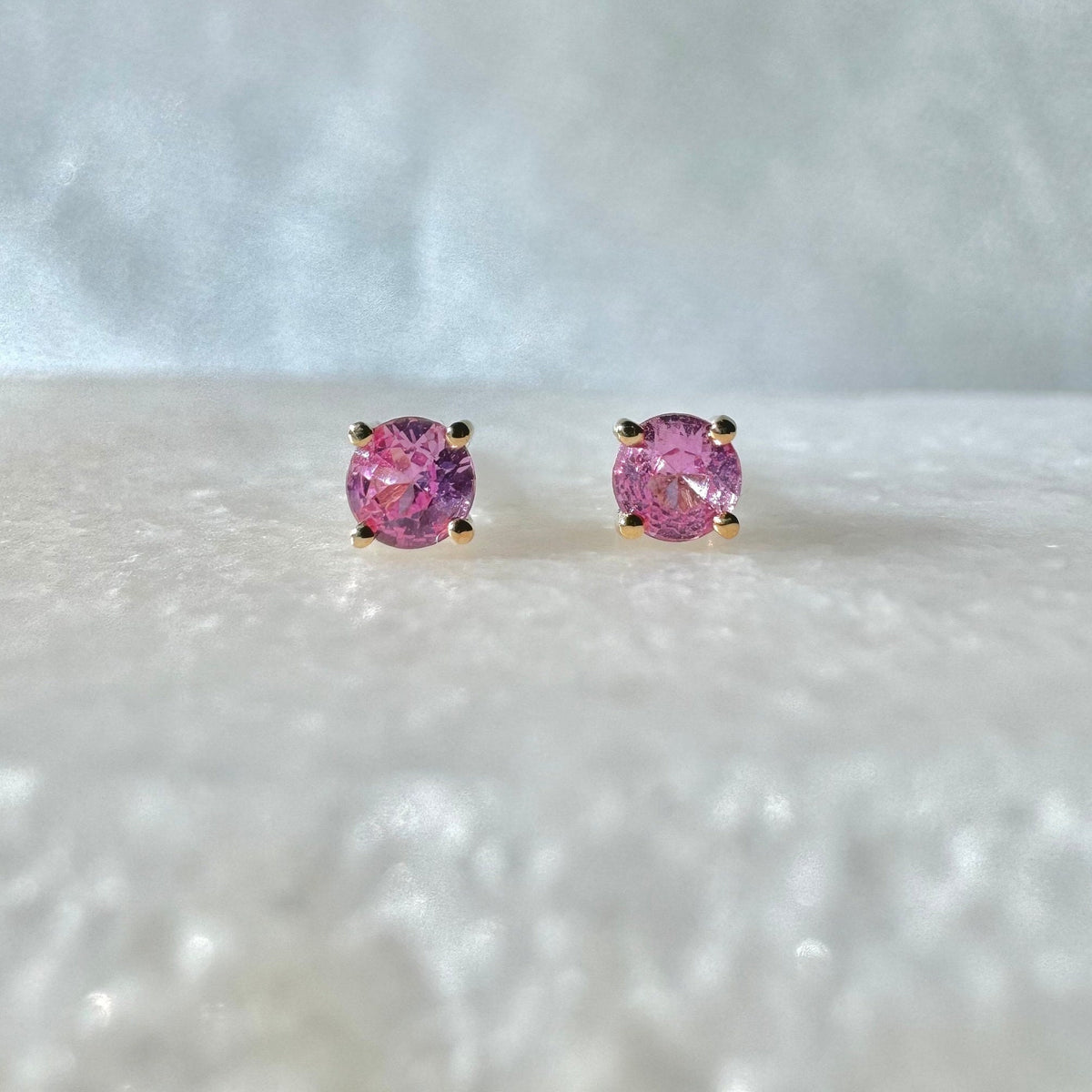 May include: A pair of gold stud earrings with pink gemstones. The earrings are set in a simple, classic style.